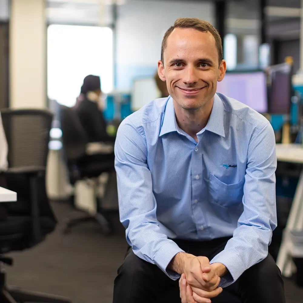 A MyBudget team member. A male individual sitting down in the office, facing the camera while smiling.