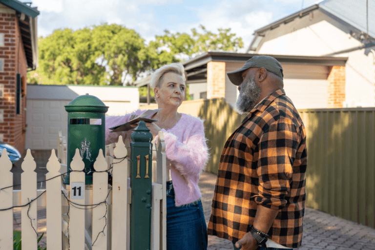 Couple discussing a bill at their front gate, representing household expenses and financial stress.